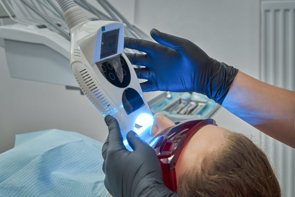 woman lying on chair during procedure of whitening of teeth